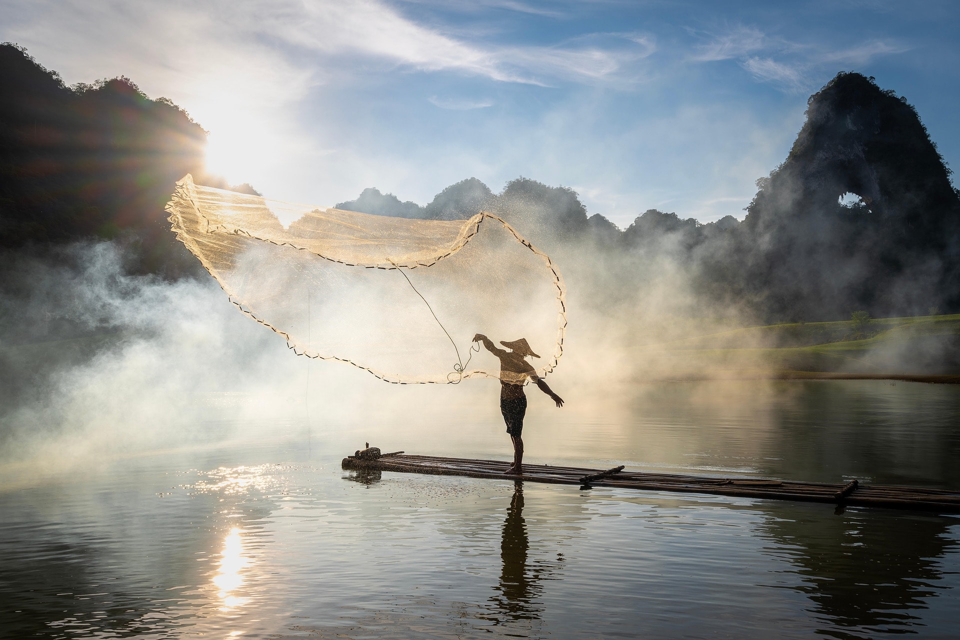 A fisherman casting a net from a small boat on open water
